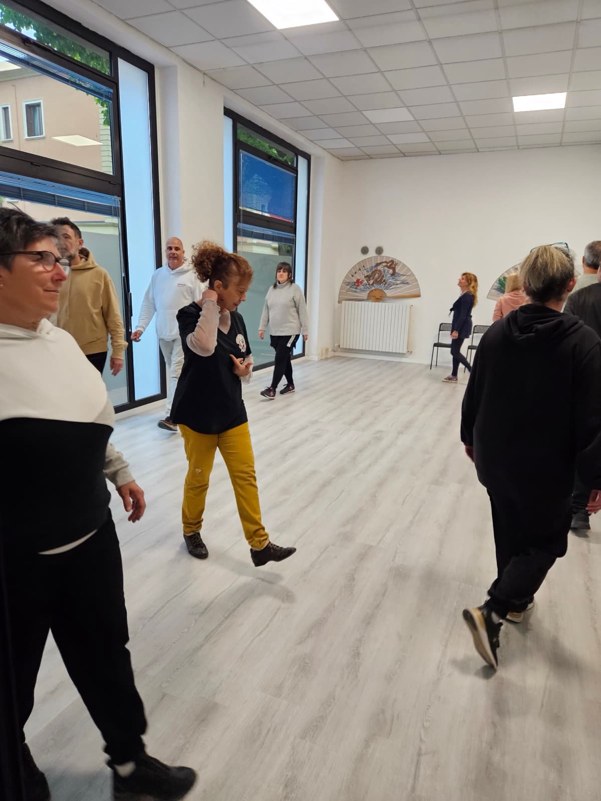Un gruppo di persone si muove a ritmo di musica in una sala, guidato dall'istruttrice